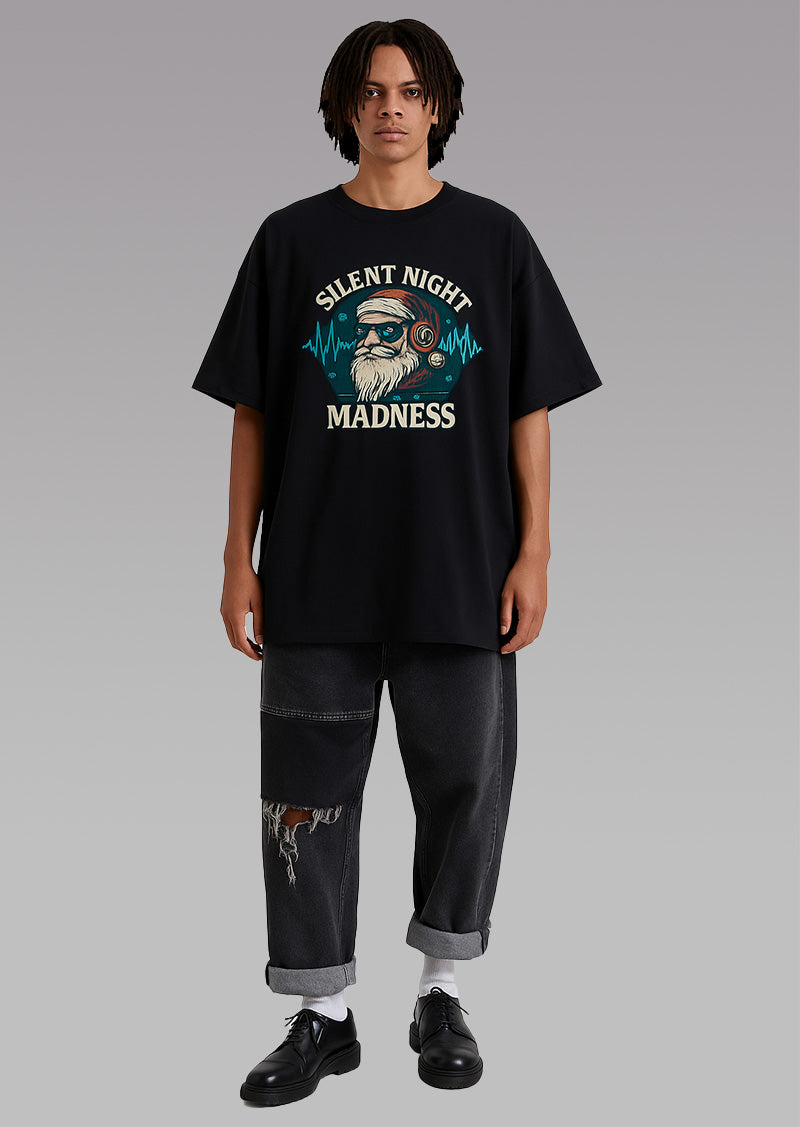 Full-length model in an oversized black graphic T-shirt with “Silent Night Madness” print, on a gray backdrop.